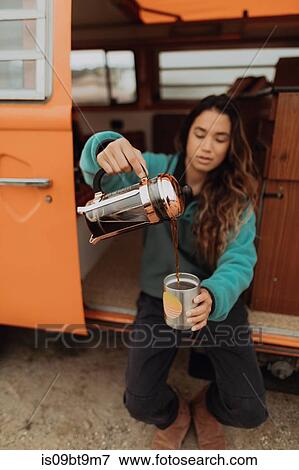 Stock Photo - Young woman pouring coffee by recreational vehicle, Jalama, California, USA. Fotosearch