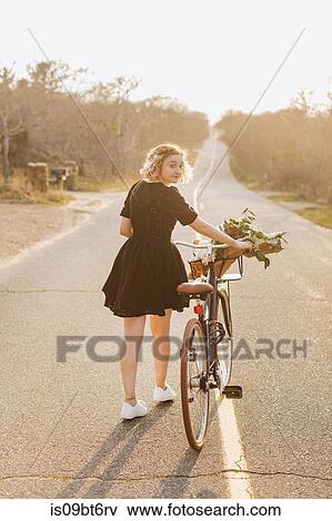 Stock Photo - Young woman pushing bicycle on rural road, rear view portrait, Menemsha, Martha's Vineyard, Massachusetts, USA. Fotosearch