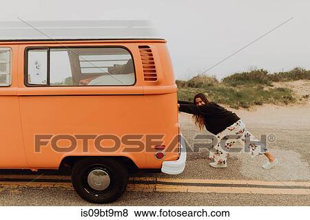 Stock Photo - Young woman pushing recreational vehicle at coastal roadside, Jalama, California, USA. Fotosearch