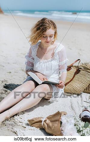 Stock Image - Young woman reading book on beach, Menemsha, Martha's Vineyard, Massachusetts, USA. Fotosearch