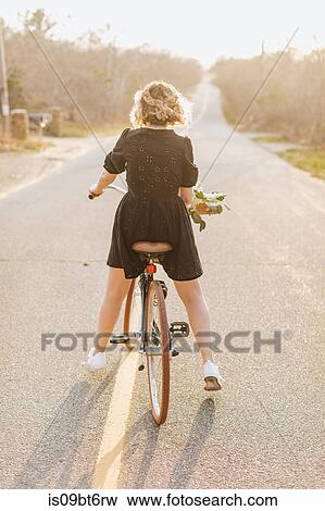 Young woman riding bicycle on rural road, rear view, Menemsha, Martha's Vineyard, Massachusetts, USA View Large Photo Image Stock Photo - Young woman riding bicycle on rural road, rear view, Menemsha, Martha's Vineyard, Massachusetts, USA. Fotosearch