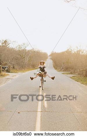 Young woman riding bicycle with legs raised on rural road, Menemsha, Martha's Vineyard, Massachusetts, USA View Large Photo Image Stock Image - Young woman riding bicycle with legs raised on rural road, Menemsha, Martha's Vineyard, Massachusetts, USA. Fotosearch
