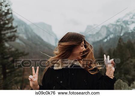 Young woman shaking long brown hair and making peace sign in mountain landscape, Yosemite Village, California, USA View Large Photo Image Stock Photograph - Young woman shaking long brown hair and making peace sign in mountain landscape, Yosemite Village, California, USA. Fotosearch