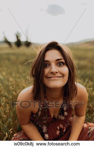 Stock Image - Young woman sitting in field of long grass pulling a face, portrait, Exeter, California, USA. Fotosearch
