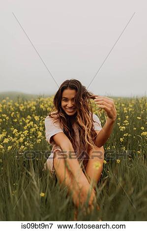 Stock Photo - Young woman sitting in yellow wildflower field, portrait, Jalama, California, USA. Fotosearch