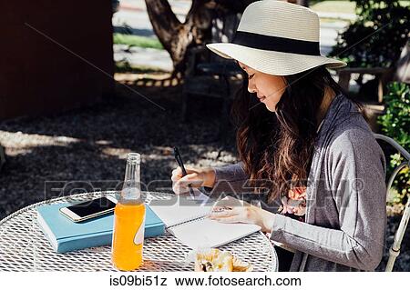 Young woman sitting outdoors, writing in notebook View Large Photo Image Stock Photo - Young woman sitting outdoors, writing in notebook. Fotosearch