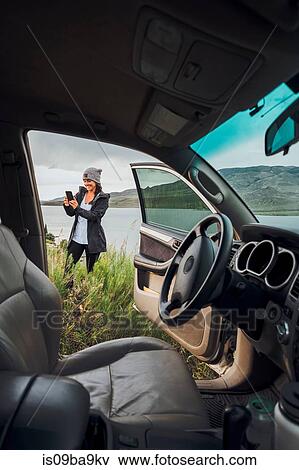 Young woman standing beside Dillon Reservoir, holding smartphone, view through parked car, Silverthorne, Colorado, USA View Large Photo Image Stock Photo - Young woman standing beside Dillon Reservoir, holding smartphone, view through parked car, Silverthorne, Colorado, USA. Fotosearch