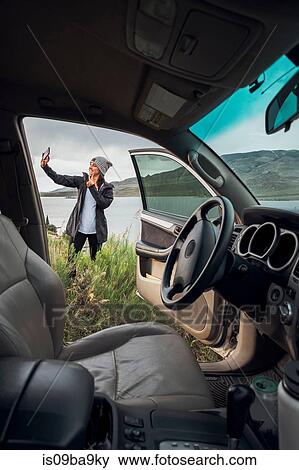 Young woman standing beside Dillon Reservoir, holding smartphone, view through parked car, Silverthorne, Colorado, USA View Large Photo Image Stock Photo - Young woman standing beside Dillon Reservoir, holding smartphone, view through parked car, Silverthorne, Colorado, USA. Fotosearch