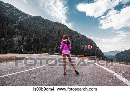 Picture - Young woman standing on mountain road with hairpin bend, Draja, Vaslui, Romania, rear view. Fotosearch