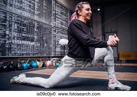 Stock Image - Young woman stretching legs in gym. Fotosearch