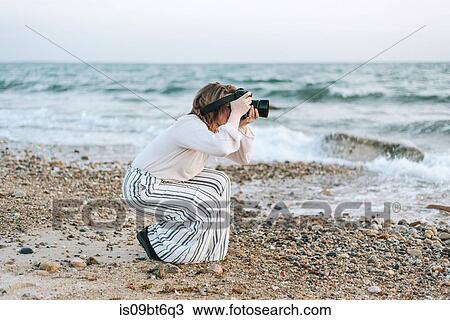 Stock Image - Young woman taking photographs from beach, Menemsha, Martha's Vineyard, Massachusetts, USA. Fotosearch