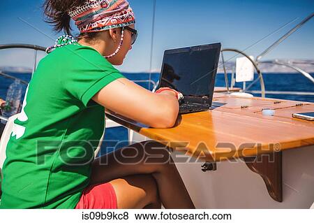 Young woman typing on laptop aboard yacht near coast, Croatia View Large Photo Image Stock Photo - Young woman typing on laptop aboard yacht near coast, Croatia. Fotosearch