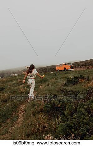 Stock Image - Young woman walking toward recreational vehicle at coast, Jalama, California, USA. Fotosearch