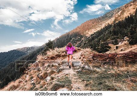 Stock Photograph - Young woman walking up dirt path mountains, Draja, Vaslui, Romania, rear view. Fotosearch