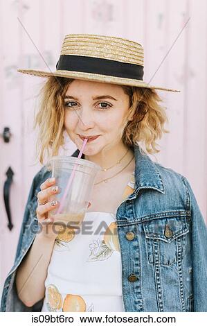 Picture - Young woman wearing boater drinking iced coffee, portrait, Menemsha, Martha's Vineyard, Massachusetts, USA. Fotosearch