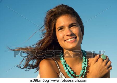 Stock Image - Young woman wearing with long brown flyaway hair against blue sky. Fotosearch