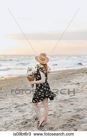 Stock Image - Young woman with bunch of flowers on windy beach, Menemsha, Martha's Vineyard, Massachusetts, USA. Fotosearch