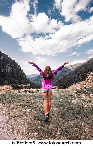 Stock Photography - Young woman with open arms looking over mountain valley, Draja, Vaslui, Romania, rear view. Fotosearch