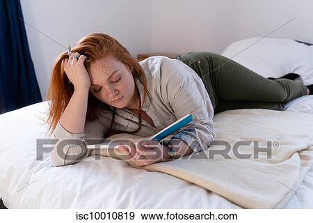 Stock Photo - Young woman with red hair lying on bed reading her diary. Fotosearch