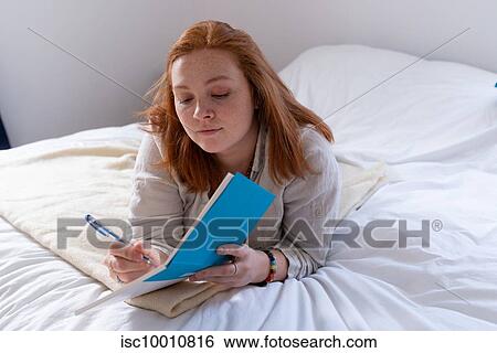 Young woman with red hair lying on bed writing in her diary View Large Photo Image Stock Photograph - Young woman with red hair lying on bed writing in her diary. Fotosearch