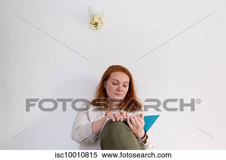 Stock Photography - Young woman with red hair sitting and reading diary at home. Fotosearch