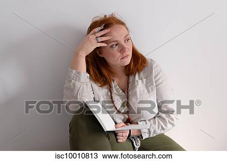Young woman with red hair sitting holding diary and looking away at home View Large Photo Image Stock Image - Young woman with red hair sitting holding diary and looking away at home. Fotosearch