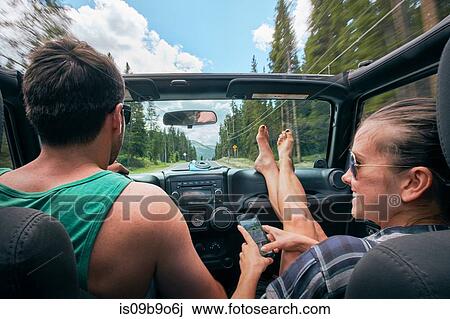 Stock Image - Young woman with smartphone driving on road trip with boyfriend, Breckenridge, Colorado, USA. Fotosearch
