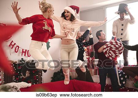 Stock Photography - Young women jumping on sofa at christmas party. Fotosearch