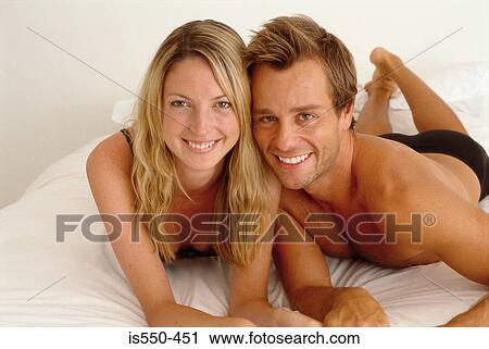 Couple lying on bed looking at camera View Large Photo Image Stock Image - Couple lying on bed looking at camera. Fotosearch