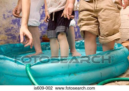 Stock Image - Family standing in paddling pool. Fotosearch