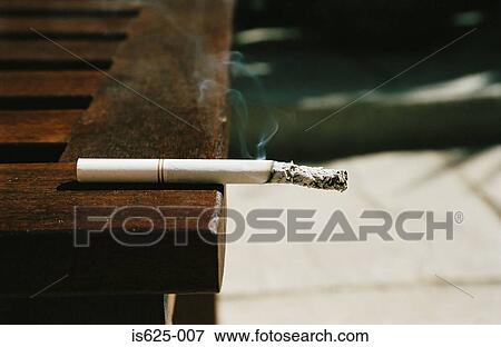 Cigarette on edge of table View Large Photo Image Stock Photo - Cigarette on edge of table. Fotosearch