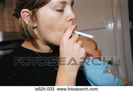 Stock Image - Woman smoking in kitchen. Fotosearch