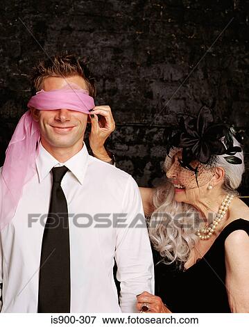 Stock Photo - Senior adult woman adjusting scarf covering young adult man's eyes. Fotosearch