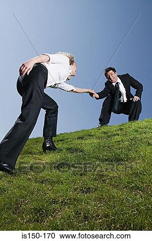 Businessman helping businesswoman up a hill View Large Photo Image Stock Image - Businessman helping businesswoman up a hill. Fotosearch