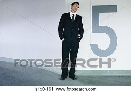 Stock Image - Businessman standing in a car park. Fotosearch