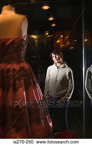 Stock Image - Woman looking at dress in shop window. Fotosearch