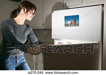 Picture - Woman looking at photograph on refrigerator. Fotosearch
