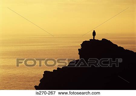 Person standing on a cliff View Large Photo Image Stock Photo - Person standing on a cliff. Fotosearch