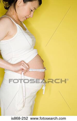 Stock Image - Pregnant woman measuring her stomach. Fotosearch