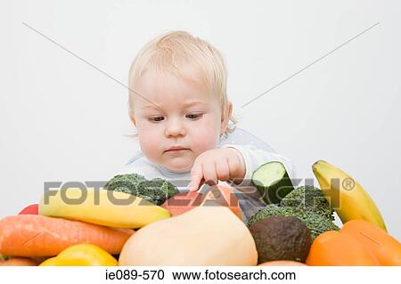 Stock Image - A baby boy looking at a stack of fruit and vegetables. Fotosearch