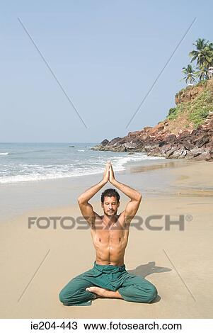 Stock Image - Man meditating on beach. Fotosearch