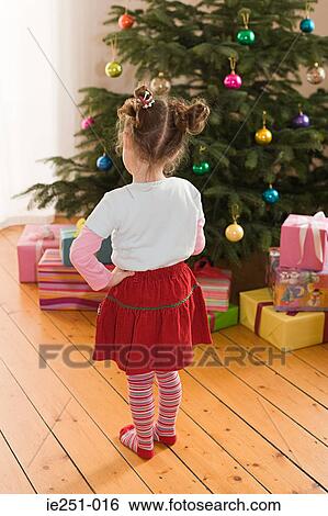 Stock Photograph - Rear view of a girl gifts and christmas tree. Fotosearch