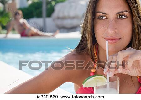 Stock Image - Woman with drink by pool. Fotosearch