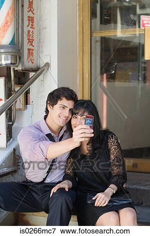 Stock Photo - A couple photographing themselves on a camera phone. Fotosearch