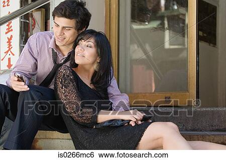 Stock Photograph - A couple sat on step using cell phone. Fotosearch