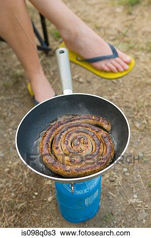 Stock Image - Sausage in camping stove. Fotosearch