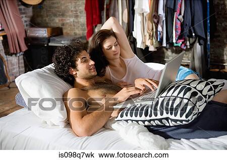 Stock Image - Couple using a laptop computer in bed. Fotosearch