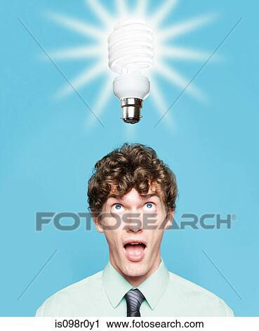 Stock Image - A young man looking at an energy saving lightbulb. Fotosearch