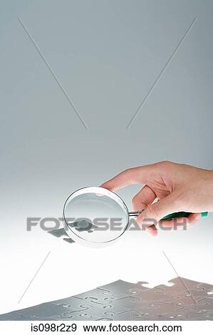 Stock Photo - Person magnifying jigsaw piece. Fotosearch