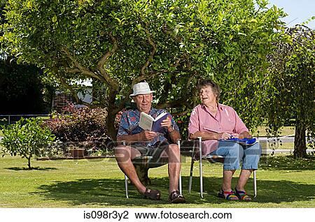 Stock Image - Senior couple relaxing under a tree in the garden. Fotosearch